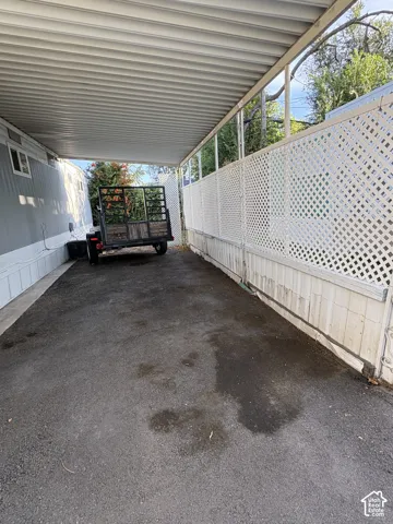 Carport featuring a corrugated metal roof, white lattice fencing, and a paved surface