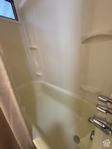 White fiberglass tub and shower combination with chrome fixtures and built-in shelving