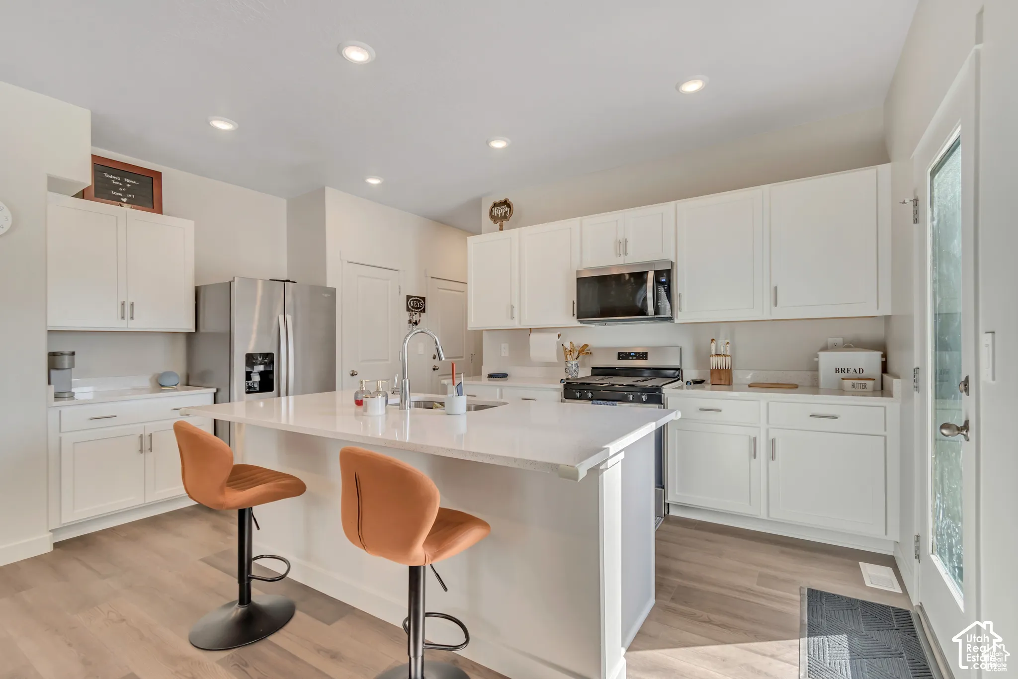 Kitchen featuring white cabinetry, stainless steel appliances, recessed lighting, wood-finish flooring, and a center island with countertop seating