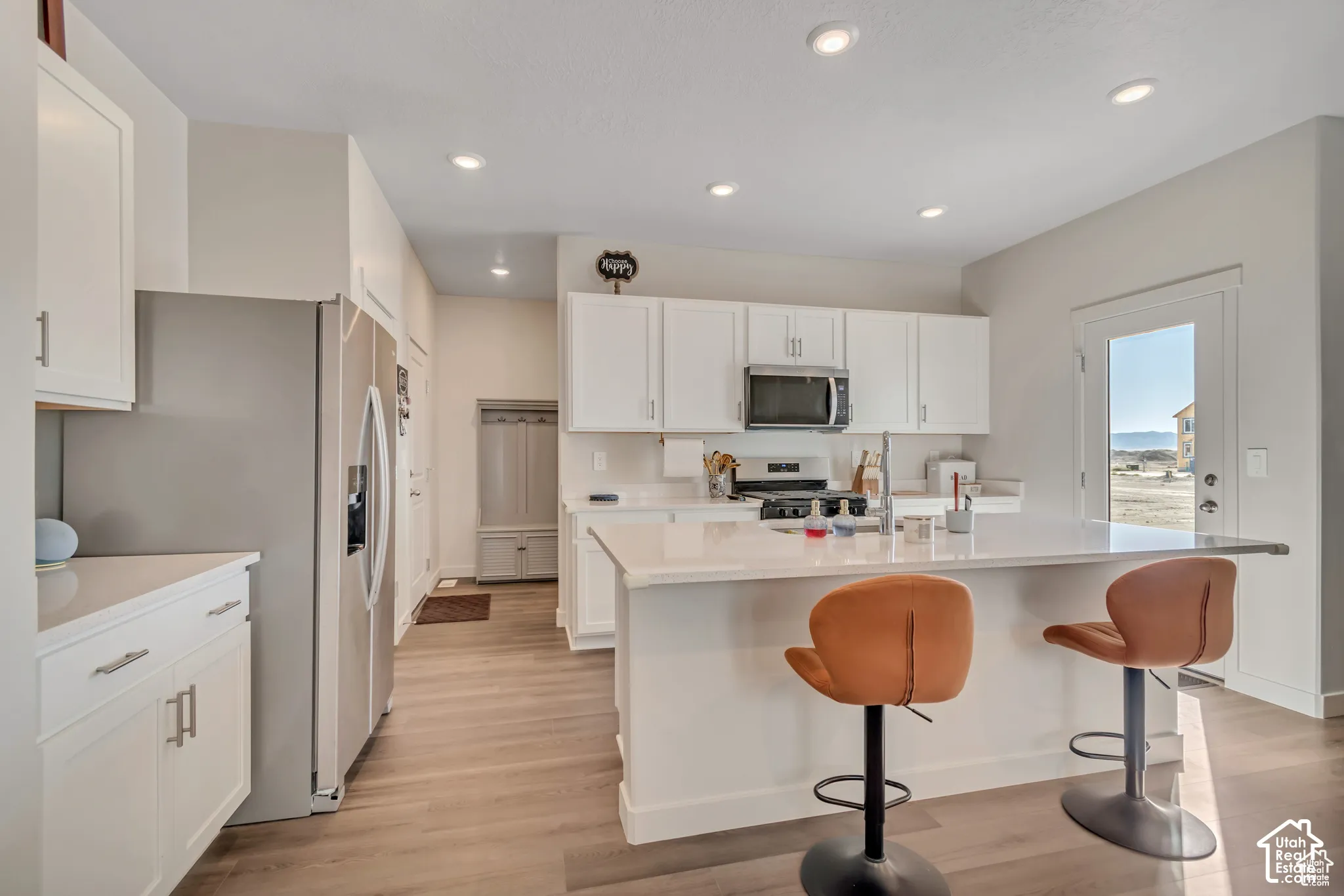 Modern kitchen featuring stainless steel appliances, recessed lighting, wood-finish flooring, white cabinetry, and a center island with countertop seating
