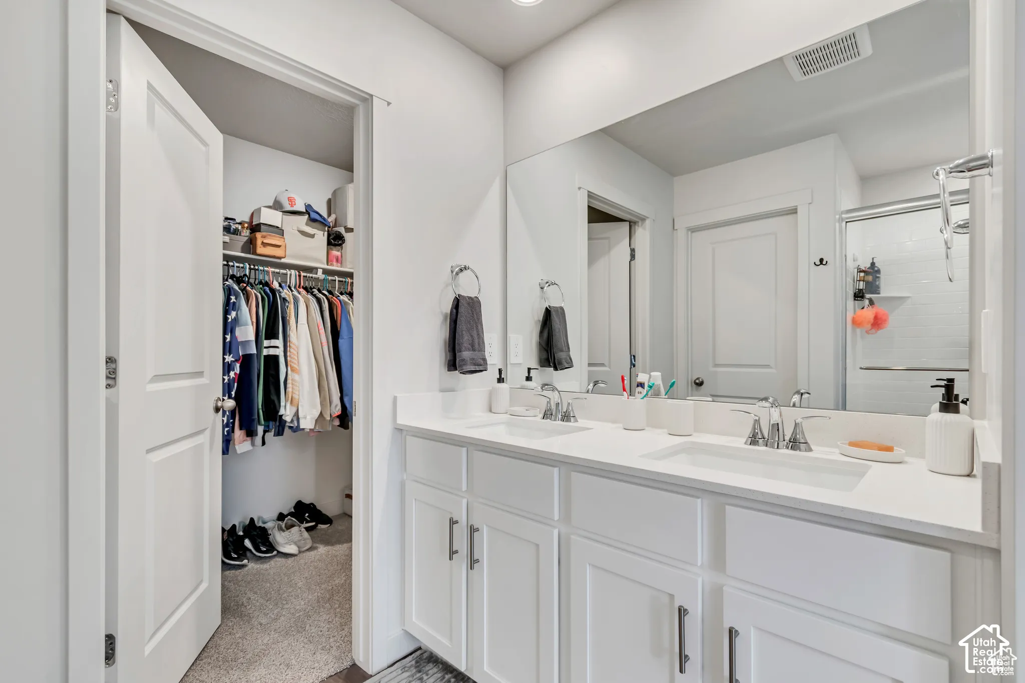 Dual vanity with white cabinetry and integrated sinks, a large wall-mounted mirror, and a walk-in closet with built-in shelving