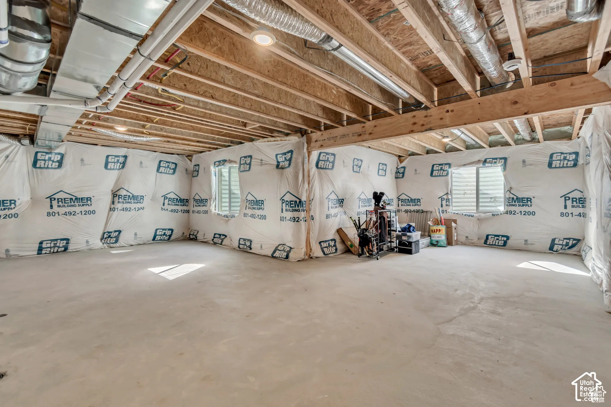 Unfinished basement with exposed ceiling joists, concrete flooring, and windows with horizontal blinds