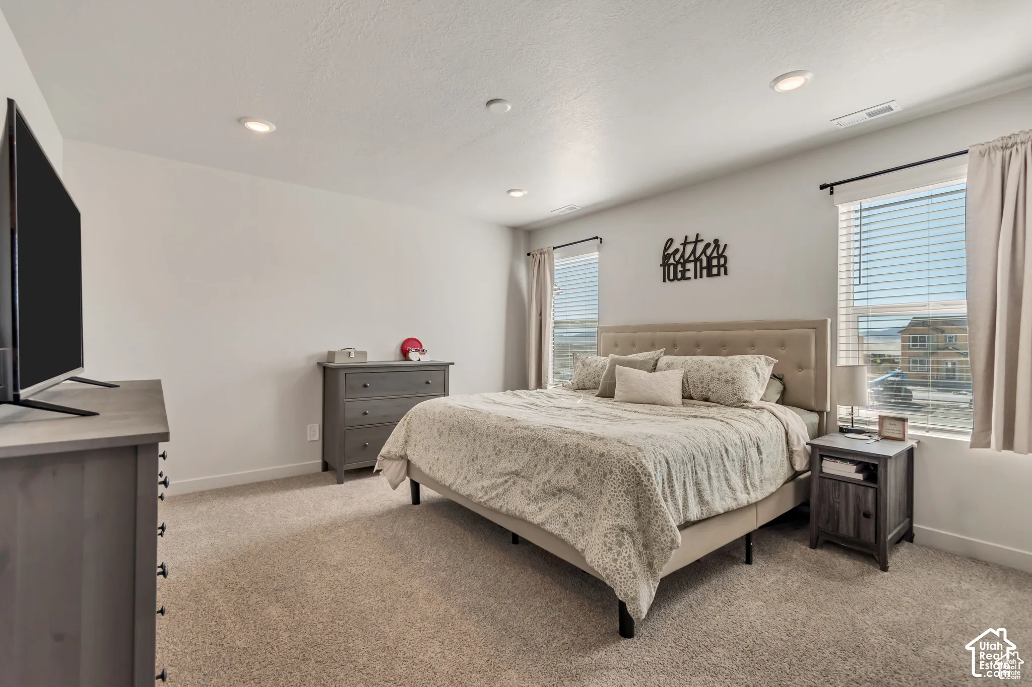 Recessed lighting, neutral wall tones, two windows with blinds, and light-toned carpeting