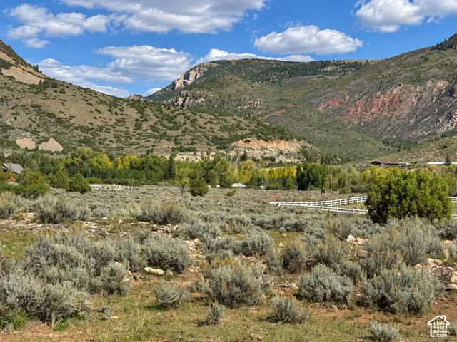 Expansive landscape featuring distant mountains, natural vegetation, and a white fence
