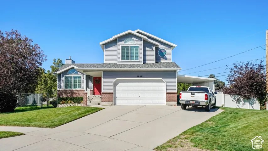 Two-story residence featuring light gray siding, a red entry door, an attached double-car garage, an arched window, and a covered carport