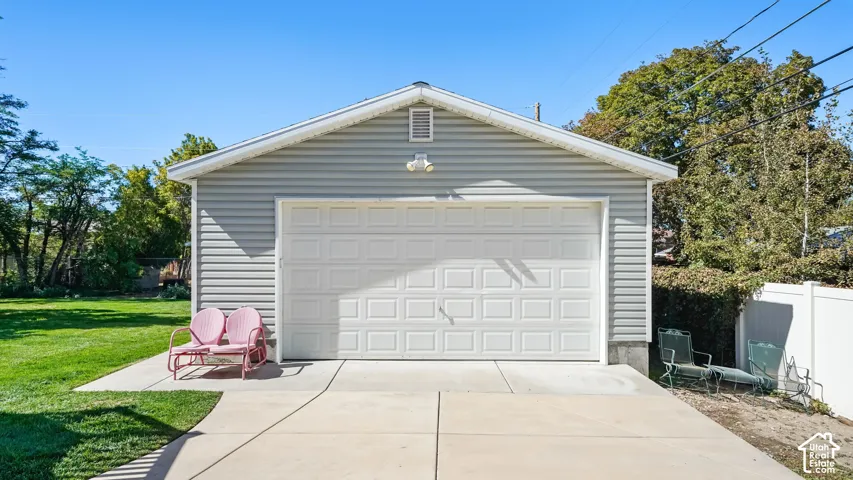 Detached garage with horizontal siding, a white panel garage door, and a concrete driveway