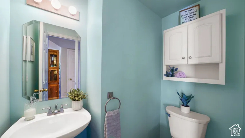 Pedestal sink with chrome faucet, beveled wall mirror, three-light vanity fixture, white wall-mounted storage cabinet