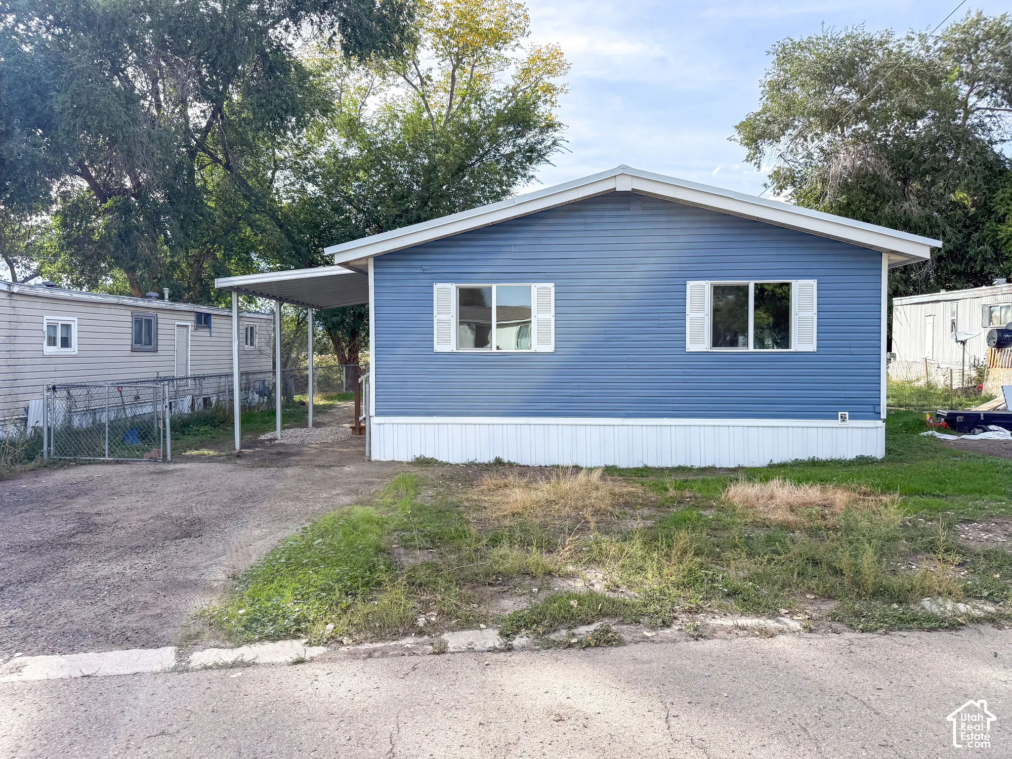 Blue horizontal siding with white trim, a covered carport, and mature trees