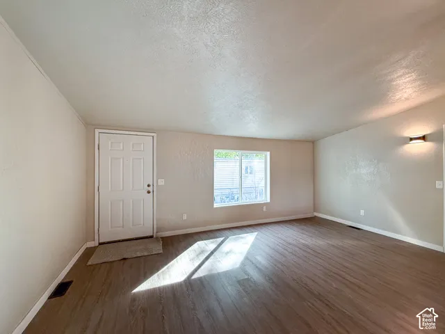 Wood-finish flooring, white paneled entry door, wall-mounted light fixture, and window with blinds