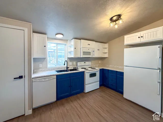 Kitchen featuring white and blue cabinetry, wood-finish flooring, and white appliances