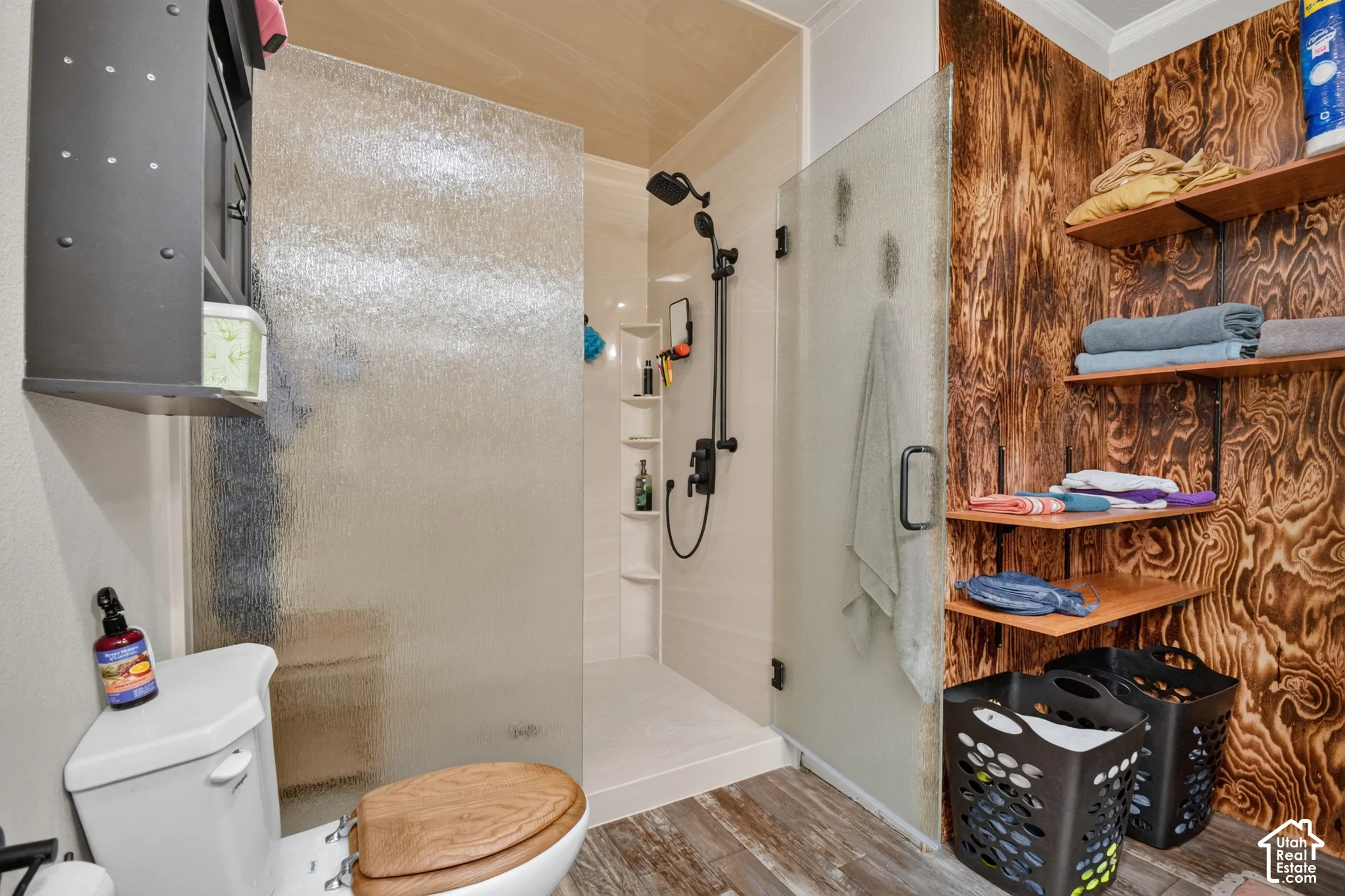 Enclosed shower with clear glass door, built-in shelving, wood-finish flooring, and open wood shelving