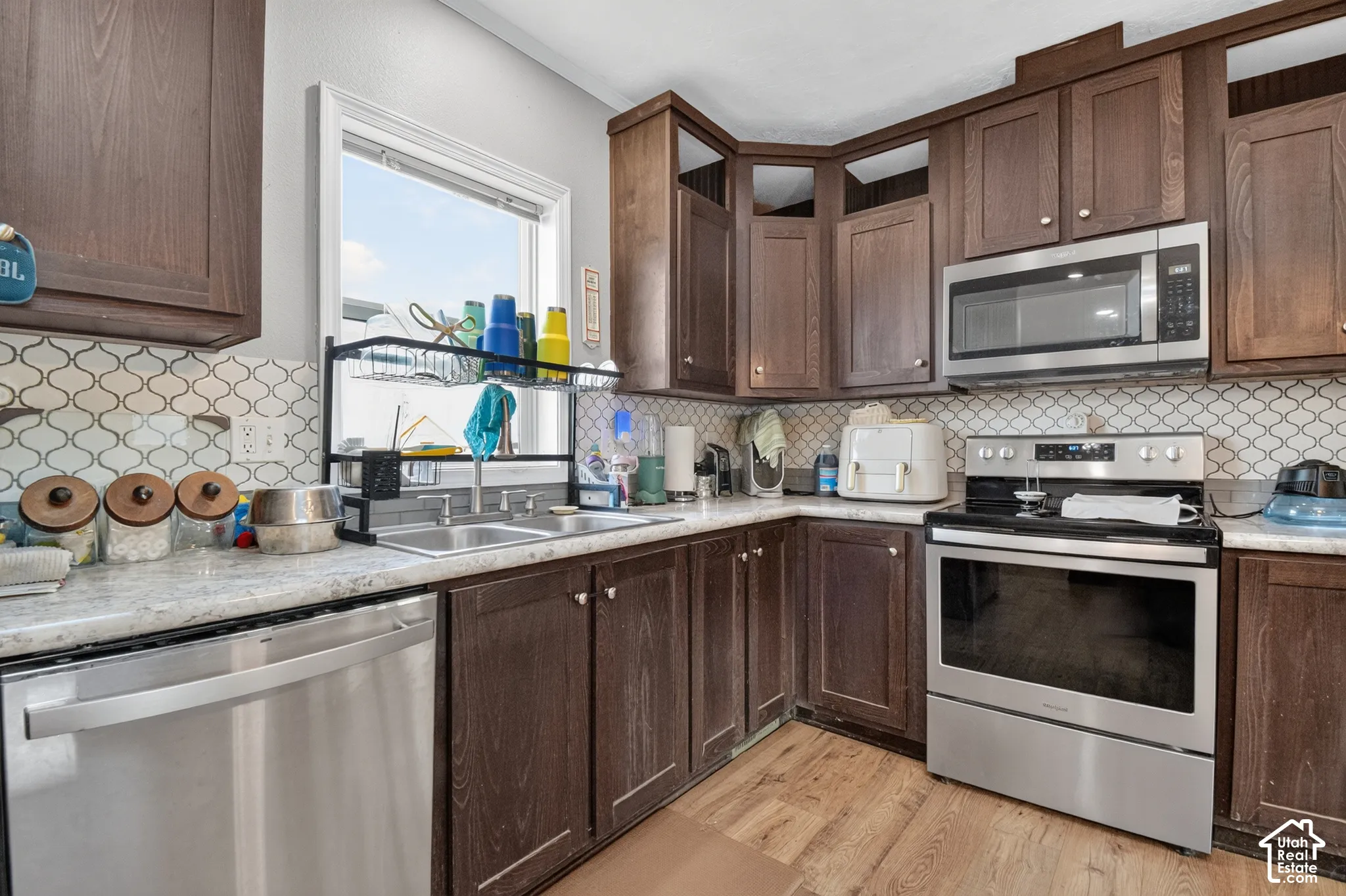 Kitchen featuring wood-finish cabinetry, stainless steel appliances, patterned tile backsplash, and light-toned countertops