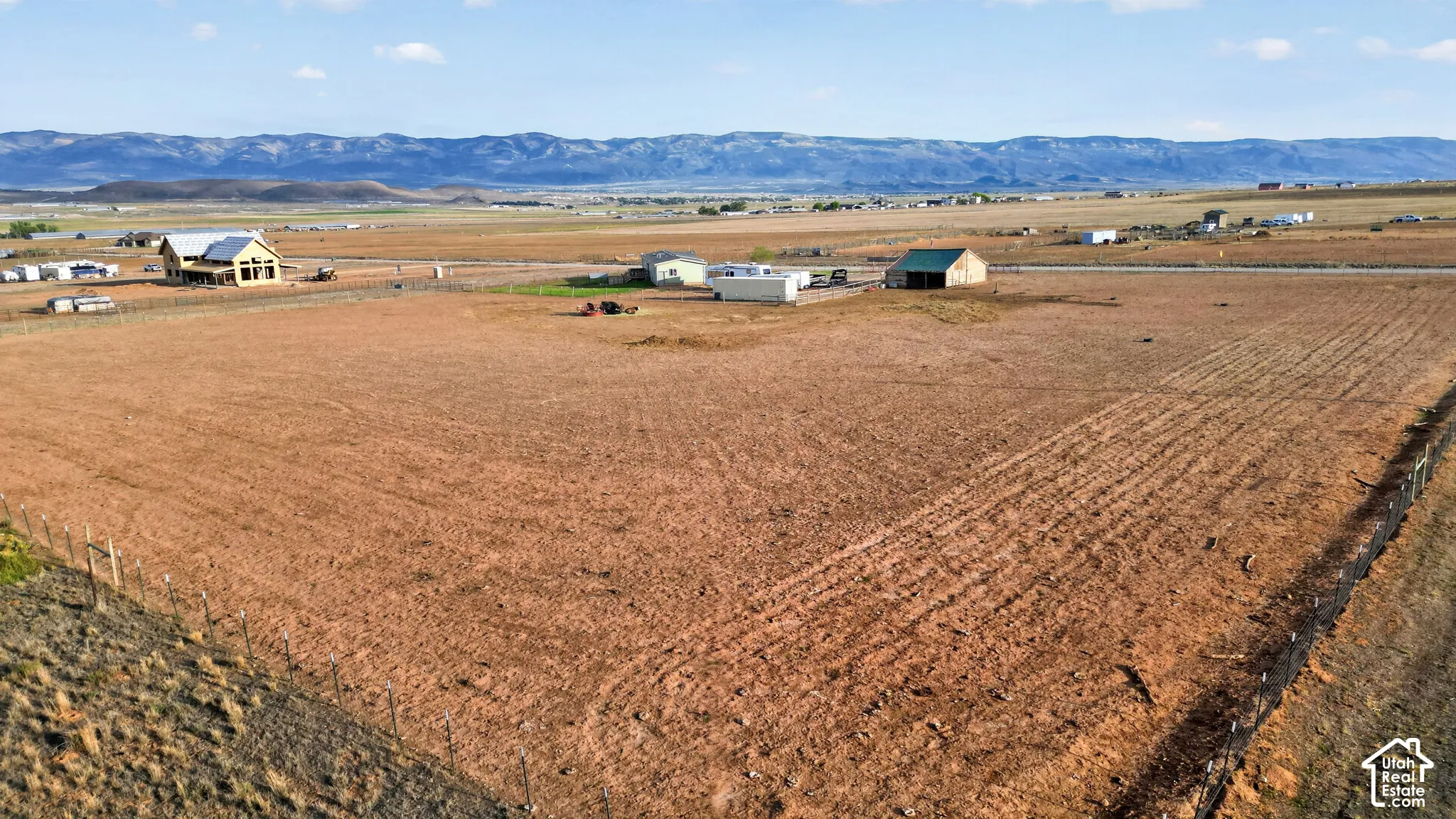 Expansive open land with distant mountain backdrop, featuring a barn structure with a green roof, and a residential building with a light-colored exterior