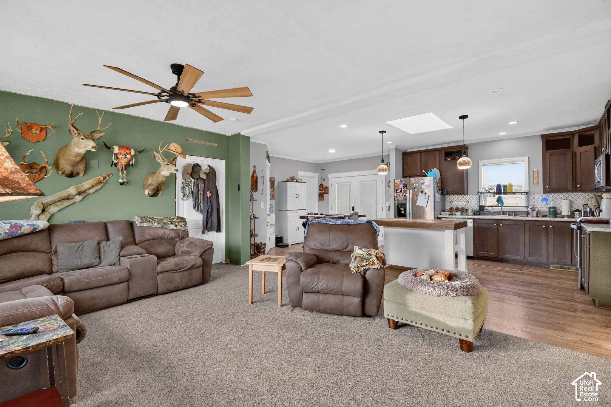 Open-concept living space featuring wood-finish flooring, a kitchen island with pendant lighting, dark wood cabinetry, and a ceiling fan