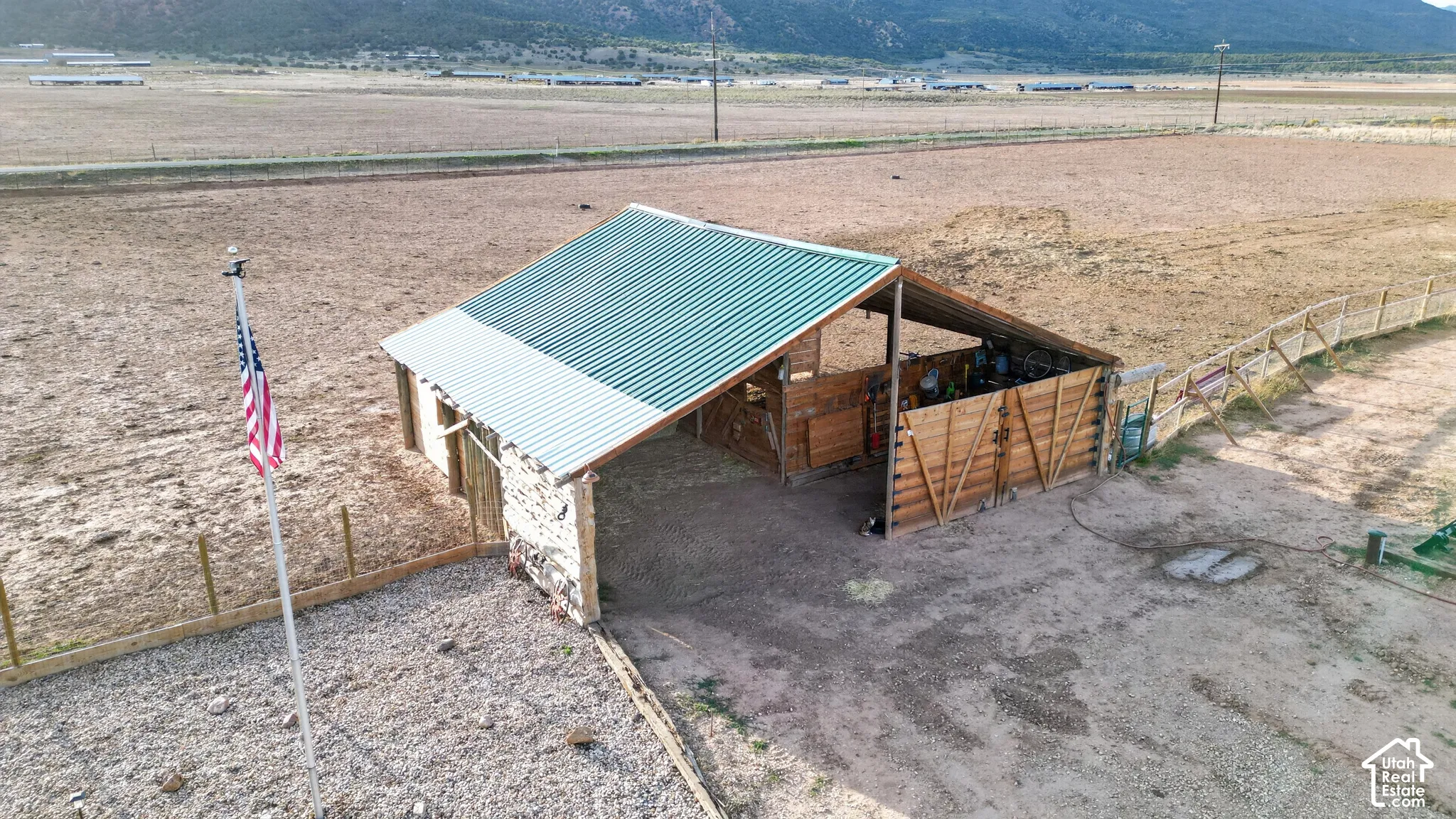 Barn structure featuring a green metal roof, partial stone wall, and wood-sided stalls