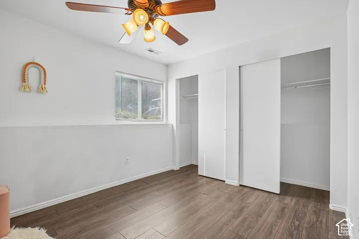 Wood-finish flooring, dual sliding door closets, window with blinds, and a ceiling fan with integrated lighting