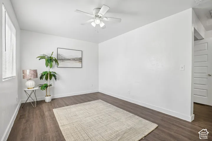 Dark wood-finish flooring, white walls, ceiling fan, and window with blinds