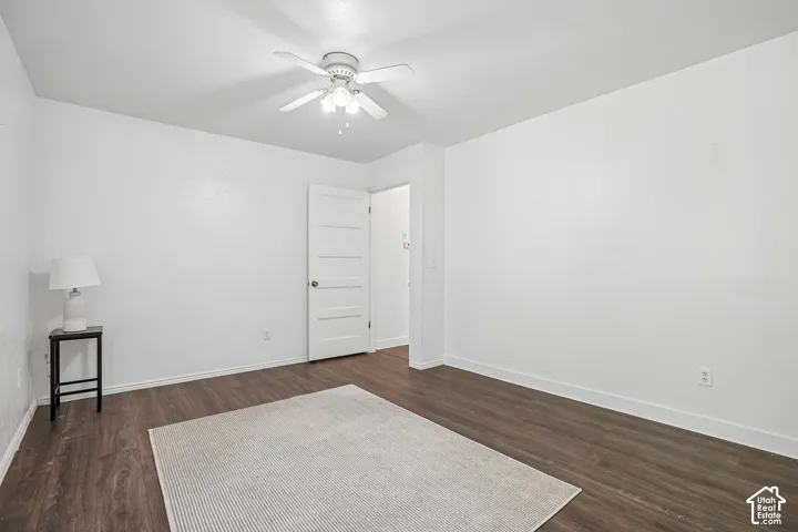 Wood-finish flooring, white paneled interior door, overhead ceiling fan, and white painted walls