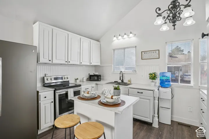 Vaulted ceiling kitchen featuring white cabinetry, stainless steel appliances, a center island with countertop seating, and wood-finish flooring