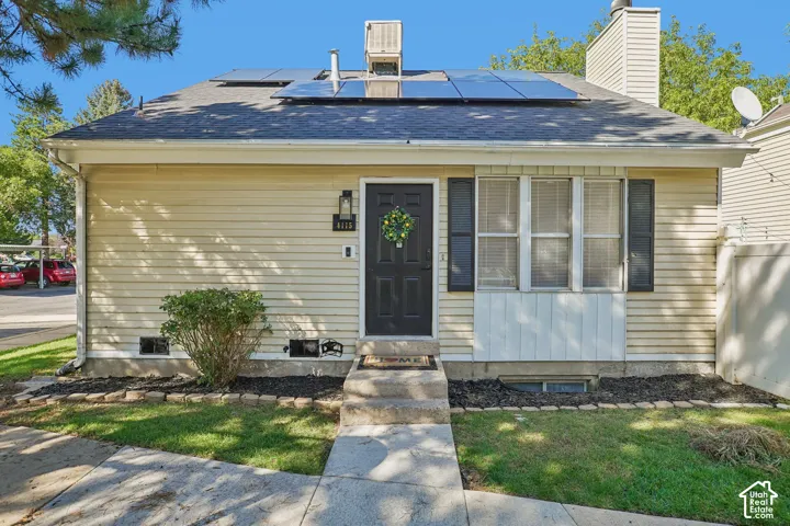 Siding exterior with a dark-paneled entry door, solar panels, and a bow window with dark shutters