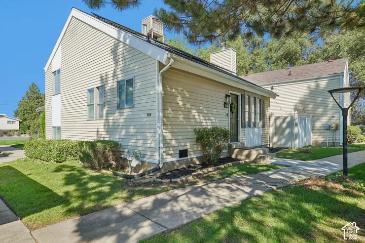 Light-colored horizontal siding, attached entry porch, concrete pathway, established shrubbery, and mature trees