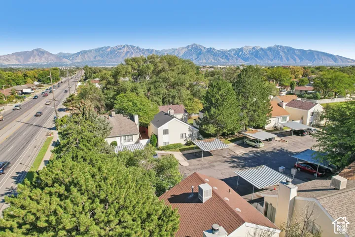 Mountain range backdrop, mature trees, multi-lane roadway, paved parking area, covered parking structures