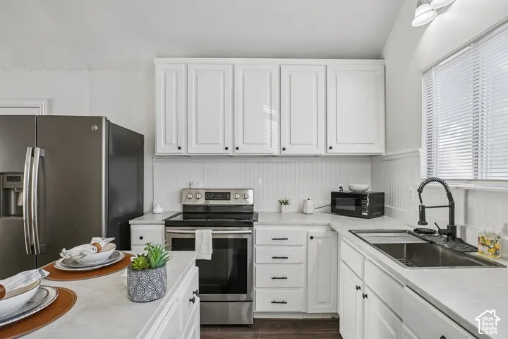White cabinetry with dark hardware, stainless steel appliances, light-toned countertops, and beadboard backsplash