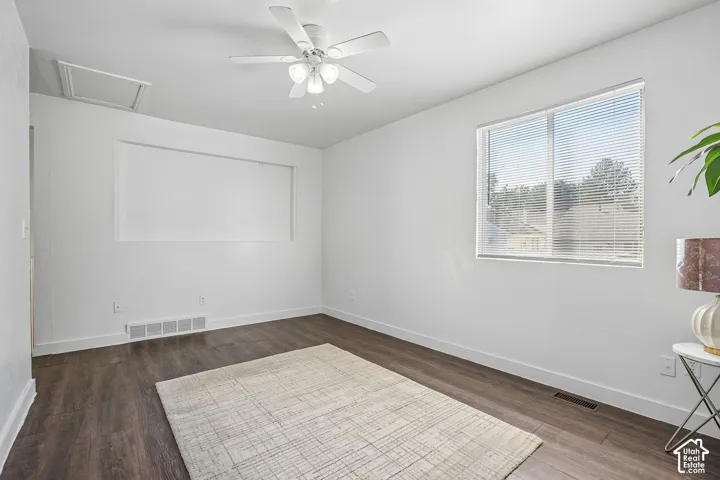 White walls, wood-finish flooring, ceiling fan with integrated lighting, recessed built-in wall feature, and a large window