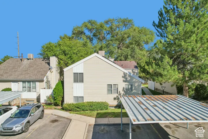 Exterior featuring light-colored siding, a pitched roof, and mature perimeter trees