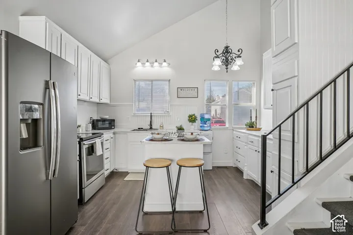 Vaulted ceiling kitchen featuring white cabinetry, stainless steel appliances, wood-finish flooring, and a central island