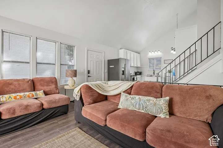 Wood-finish flooring throughout the living space, vaulted ceilings, and a kitchen featuring white cabinetry and stainless steel appliances