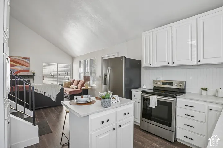 Vaulted ceiling, wood-finish flooring, white cabinetry, stainless steel appliances, and white countertops