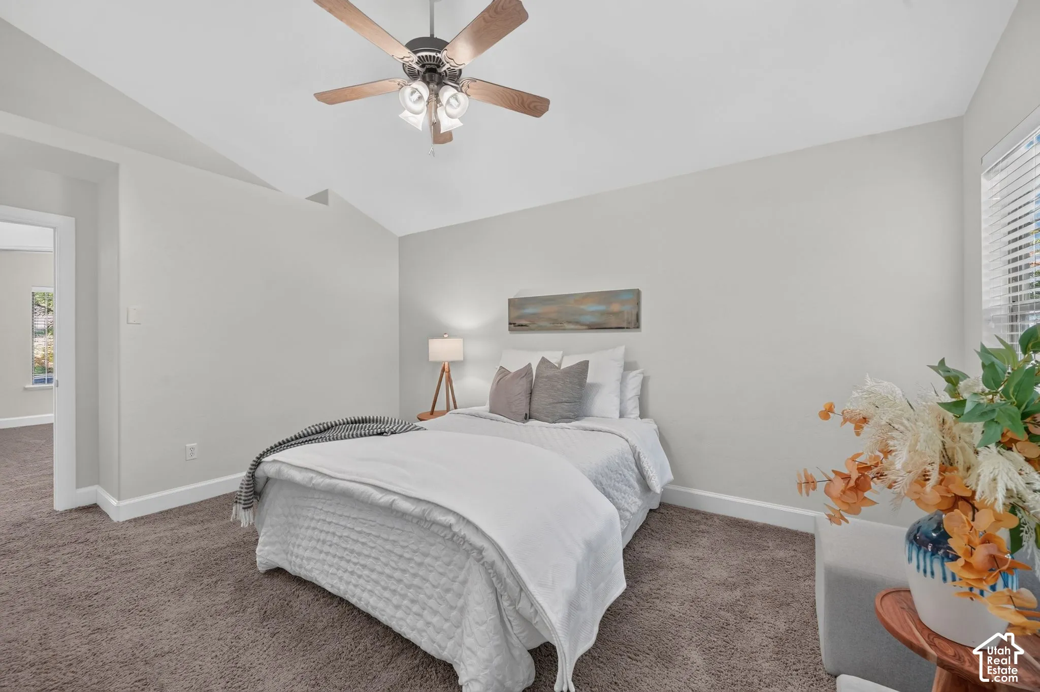 Vaulted ceiling, ceiling fan with integrated lighting, window with blinds, light gray wall paint, and gray carpet flooring