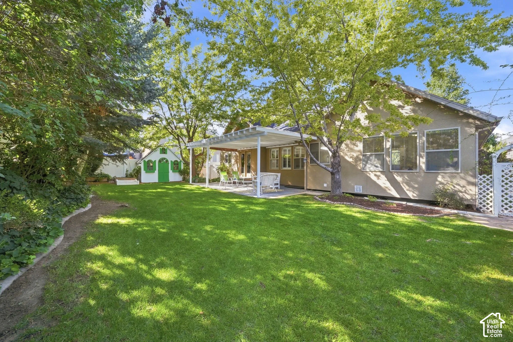 Expansive manicured lawn with mature trees, covered patio with structural columns, and a charming detached shed