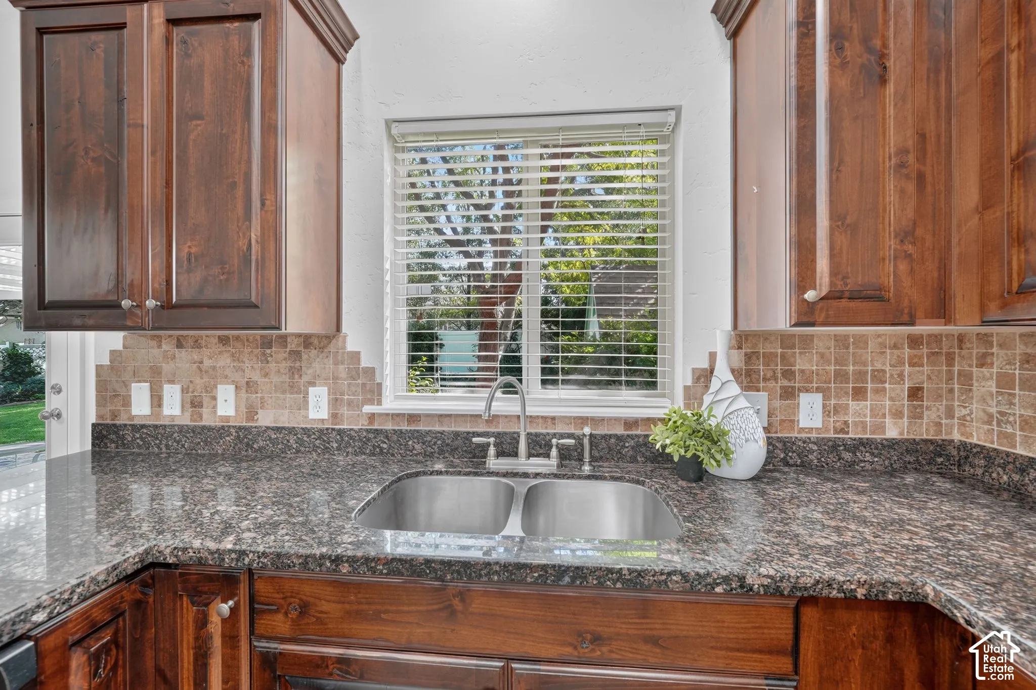 Rich wood cabinetry with crown molding, speckled stone countertops, and a tile backsplash