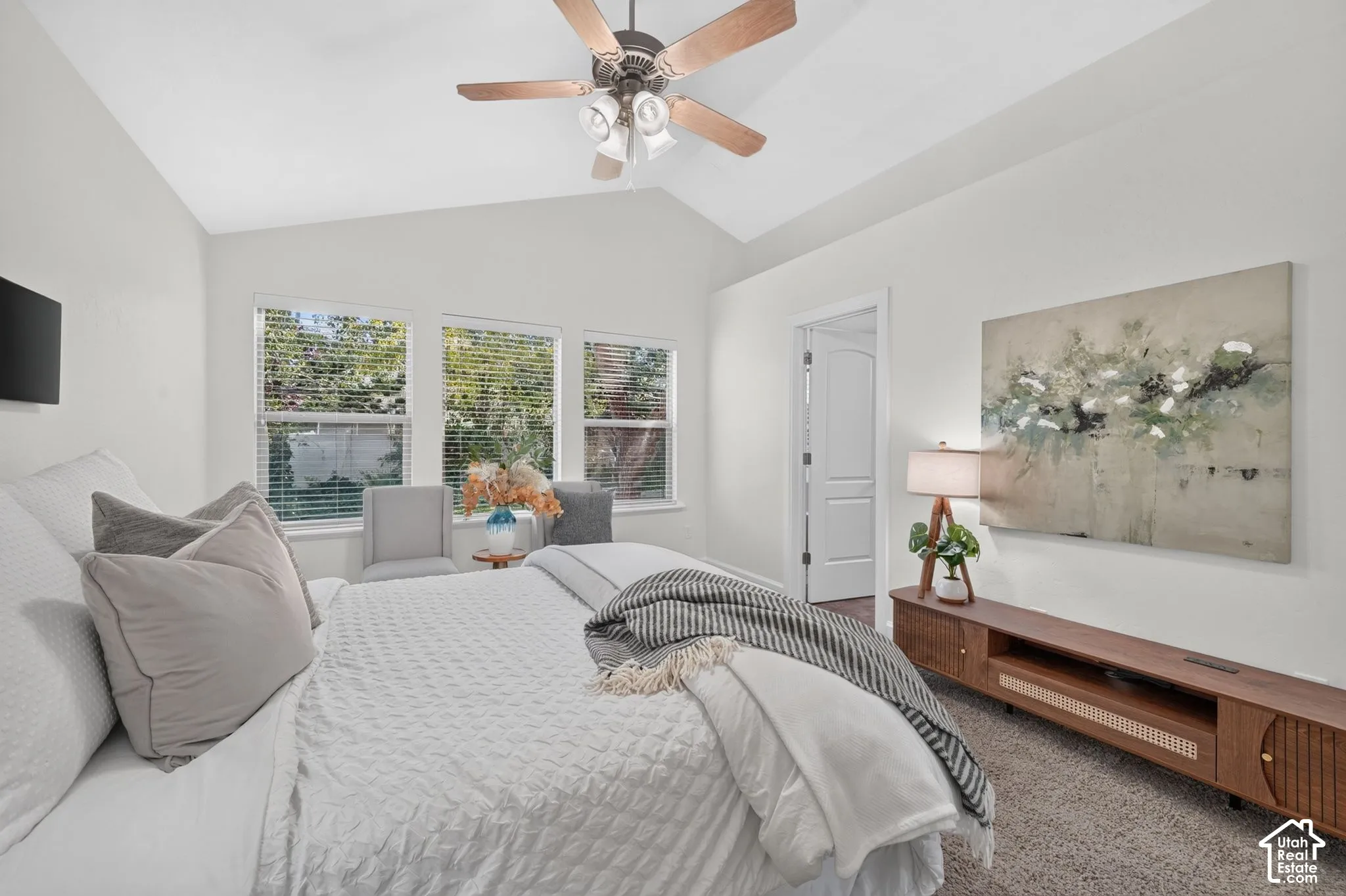 Vaulted ceiling with a ceiling fan, three windows with blinds, light-colored walls, and neutral carpeting