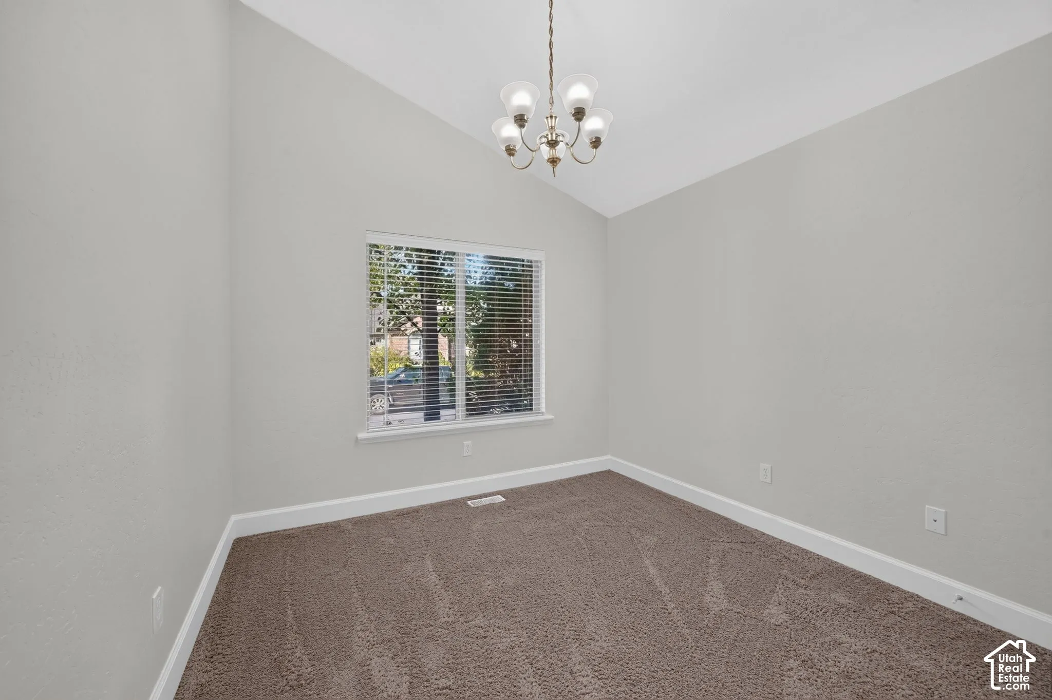 Vaulted ceiling, neutral wall paint, bronze chandelier, window with blinds, and carpeting