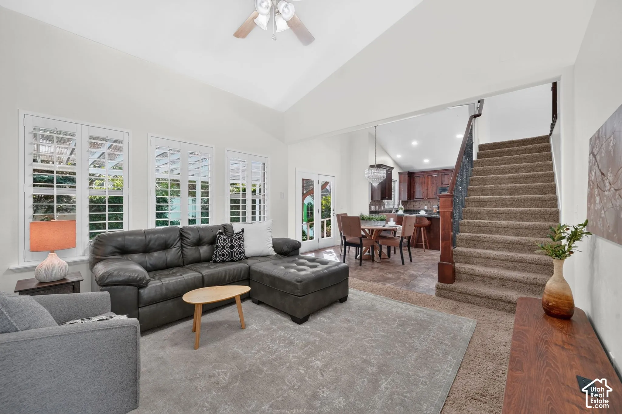 Vaulted ceiling, three large windows with plantation shutters, staircase with wood banister, recessed lighting, and a chandelier-style fixture