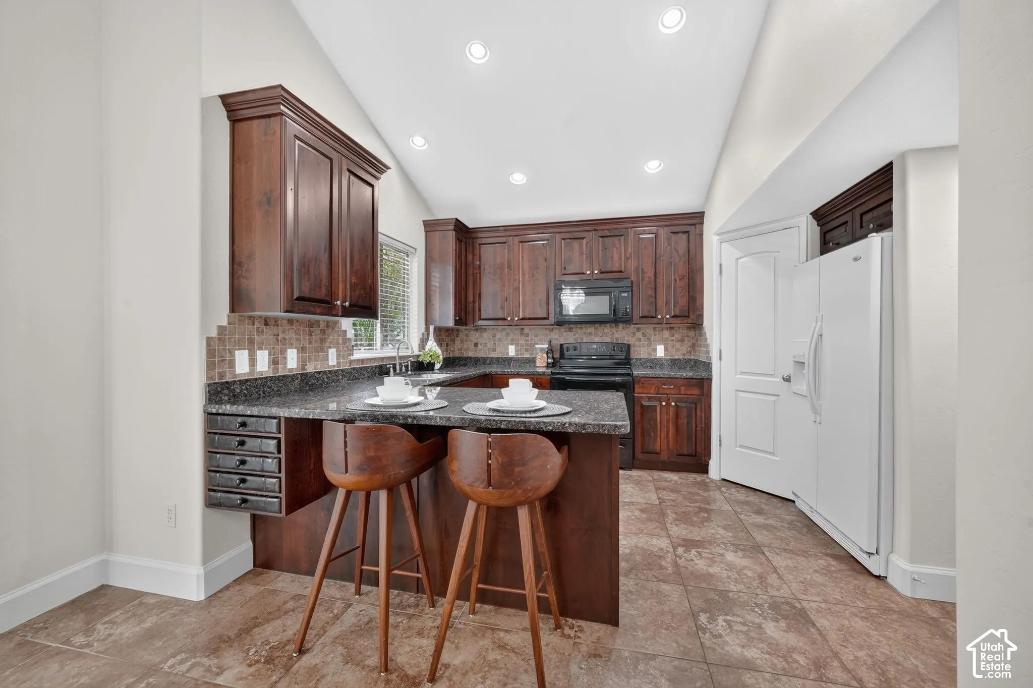 Kitchen featuring dark wood cabinetry, a breakfast bar with stone-finish countertops, tile backsplash, and recessed lighting