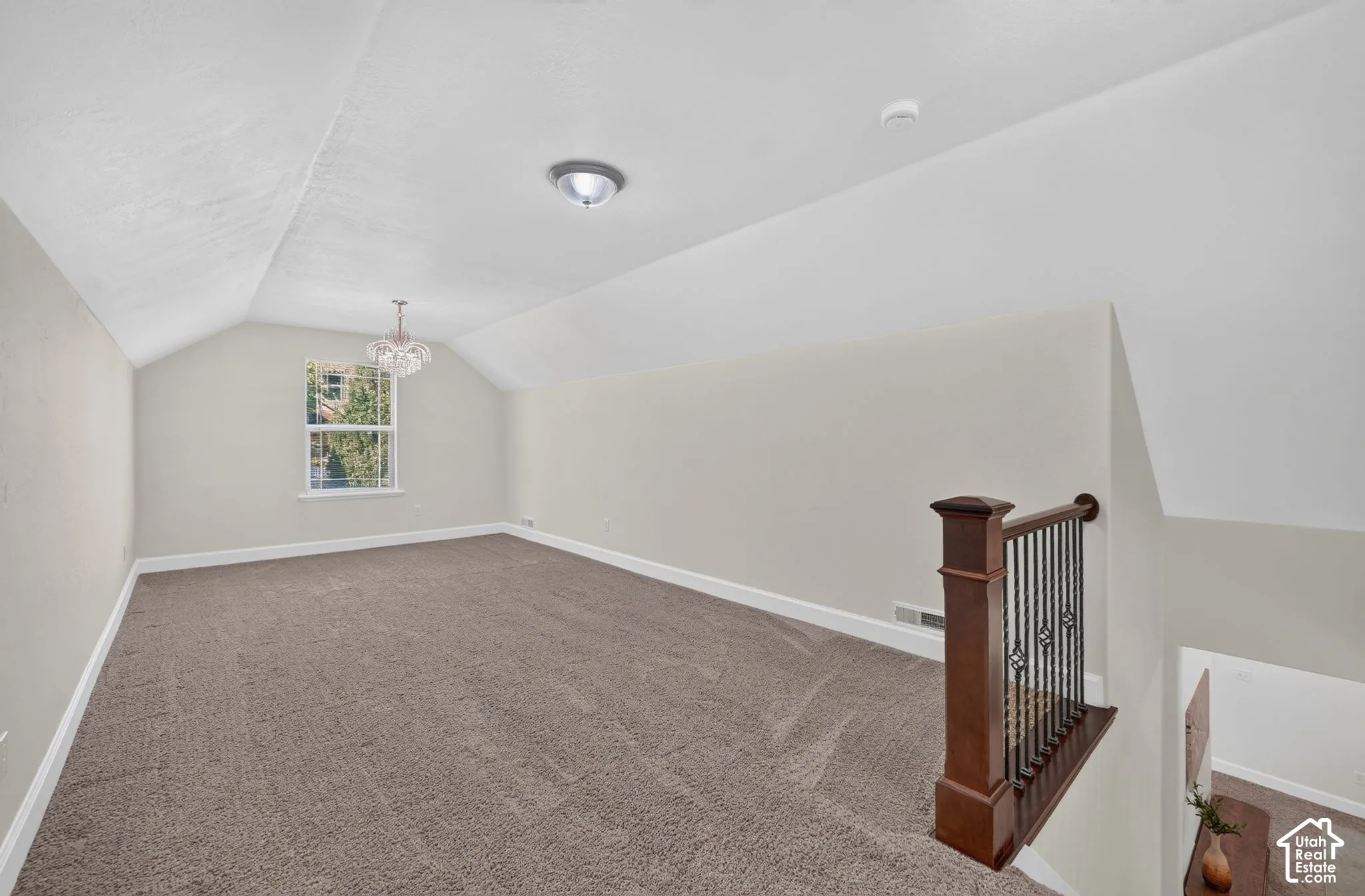 Vaulted ceiling loft with carpeted flooring, a decorative chandelier, and a wood and wrought iron banister