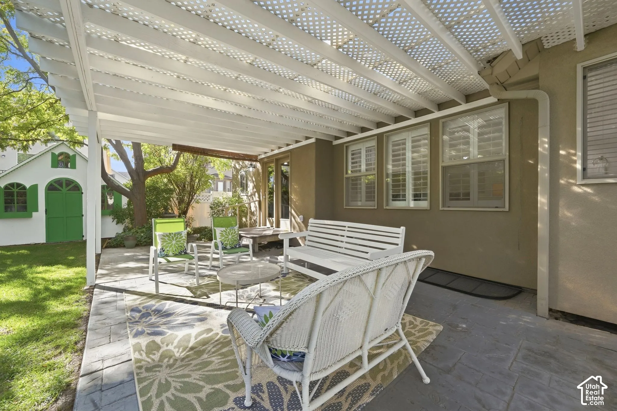 Covered patio with a lattice roof, featuring a paver stone surface, and an exterior wall with multiple windows