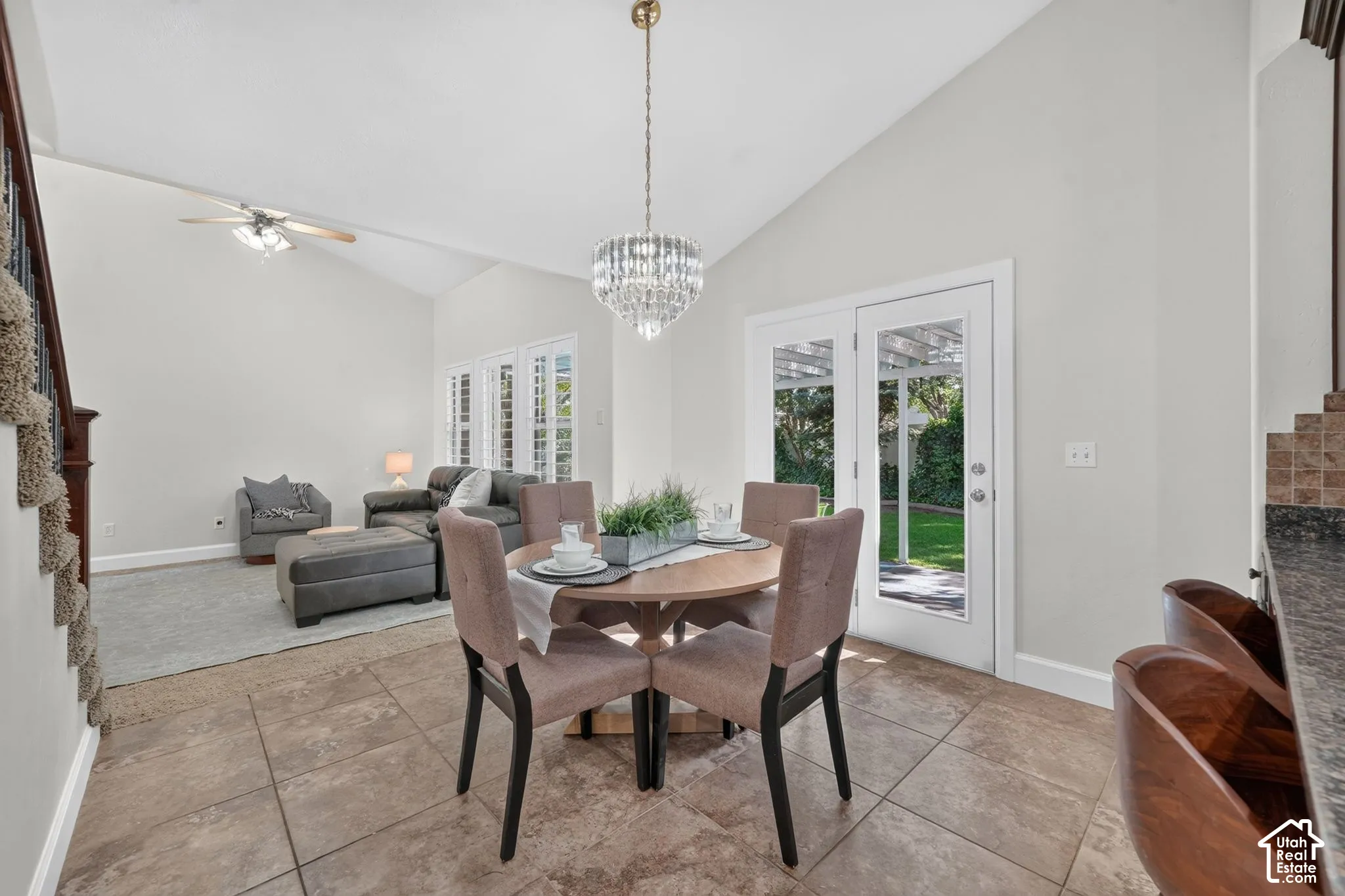 Vaulted ceiling with a ceiling fan, French doors, plantation shutters, tiled flooring, and a crystal chandelier