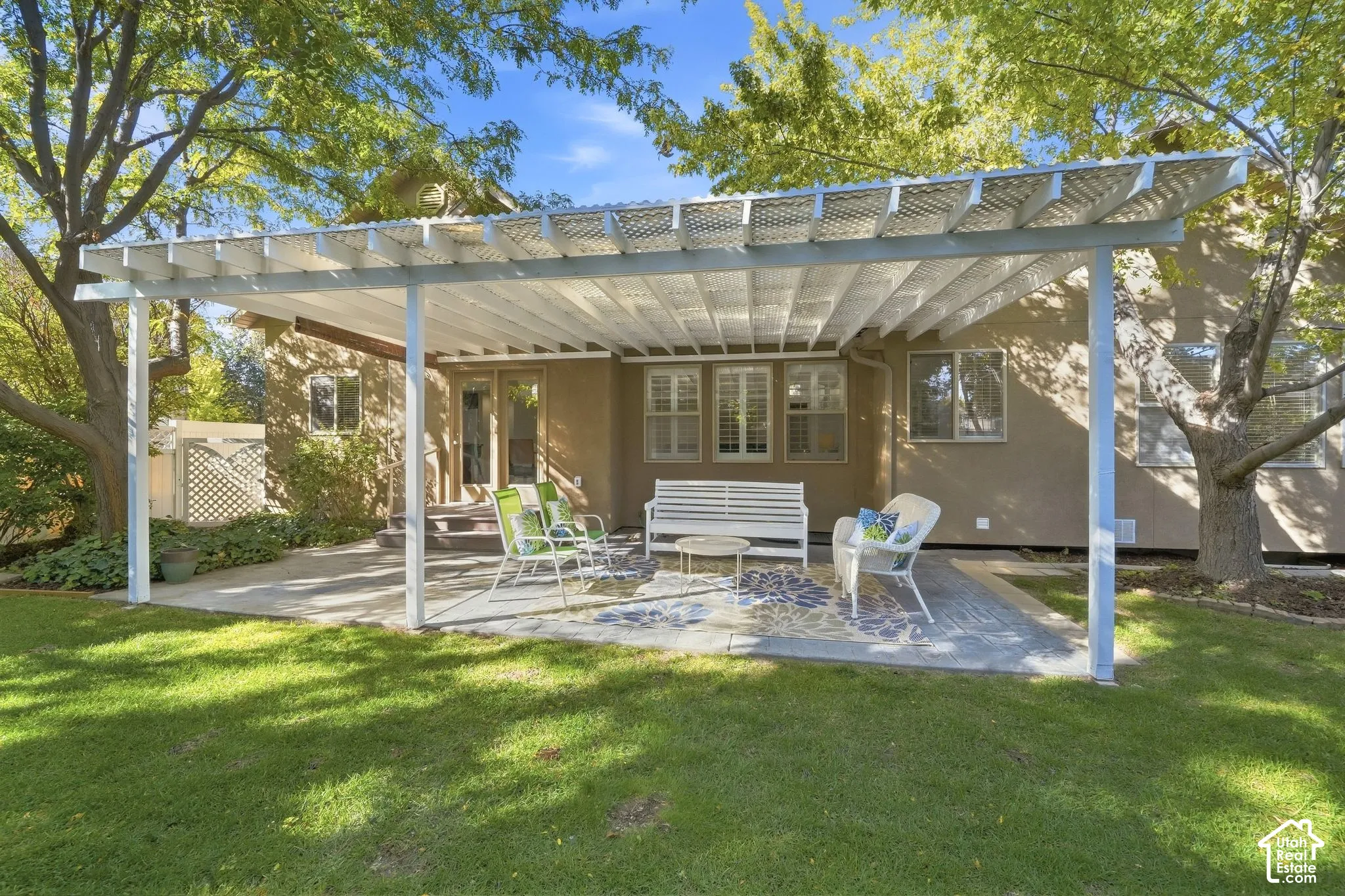 Expansive patio featuring a white pergola structure, concrete paving, and a manicured lawn