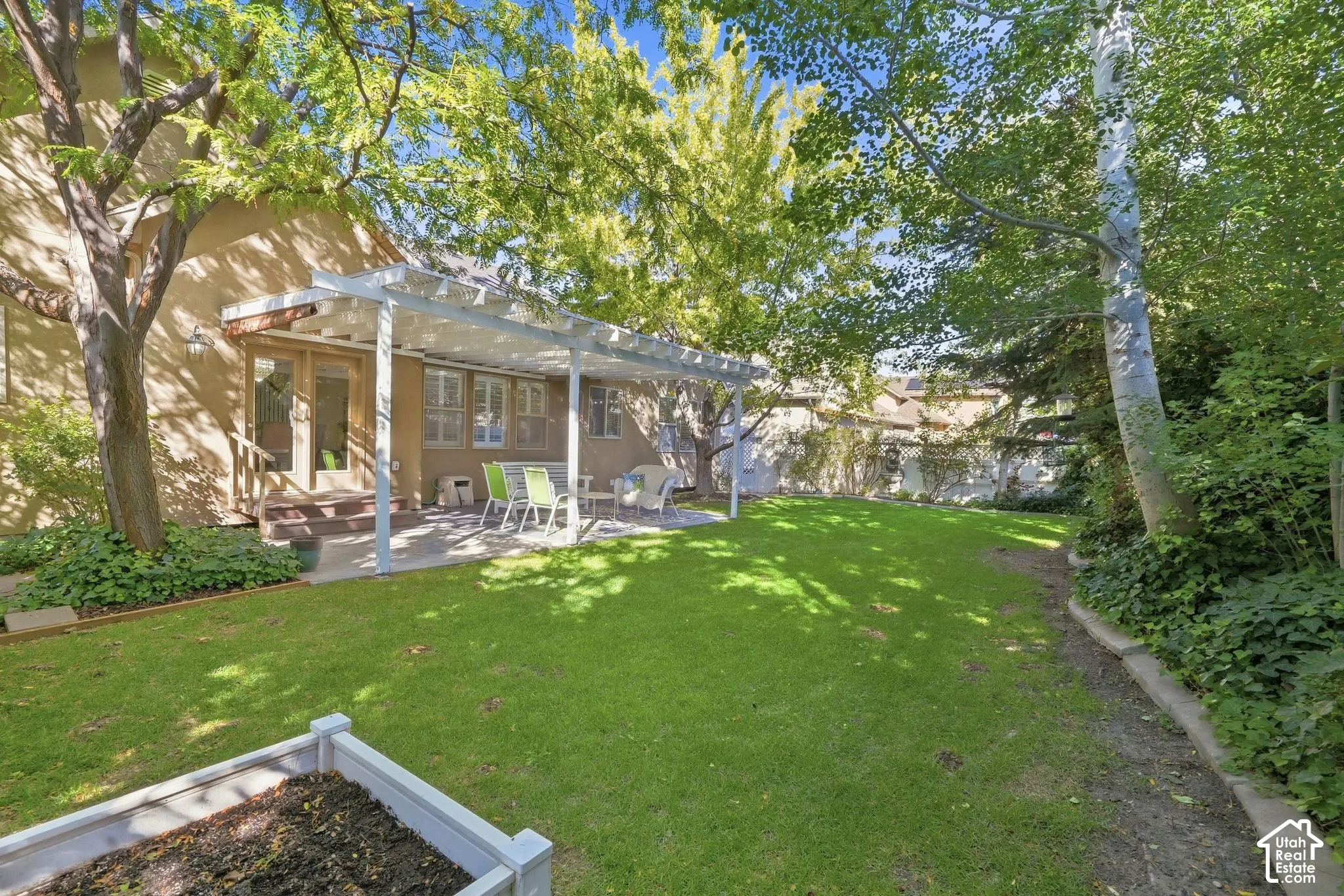 Expansive backyard featuring a manicured lawn, mature trees, and a covered patio with a concrete surface