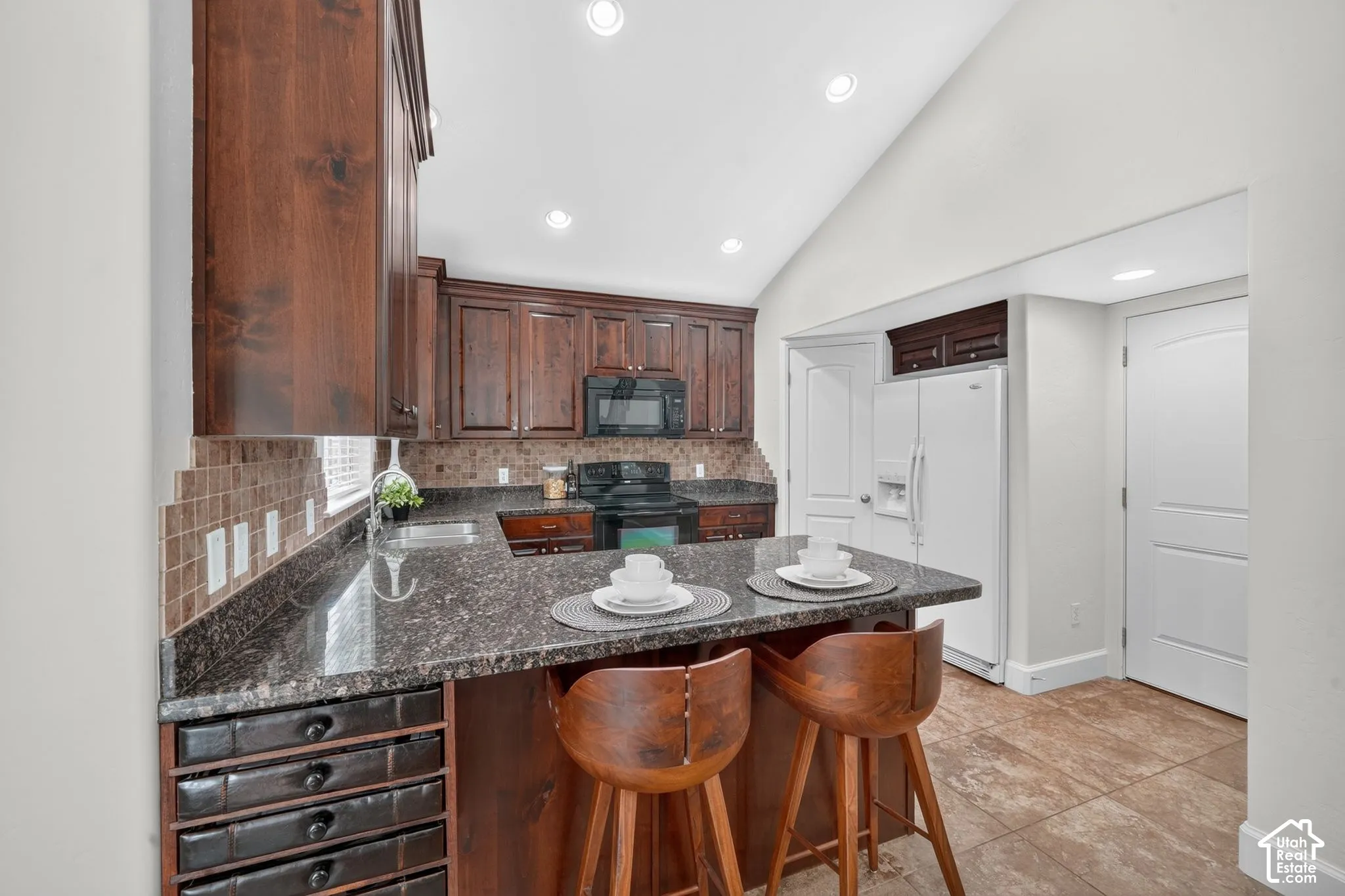 Kitchen featuring wood cabinetry, granite countertops, tile backsplash, and a vaulted ceiling