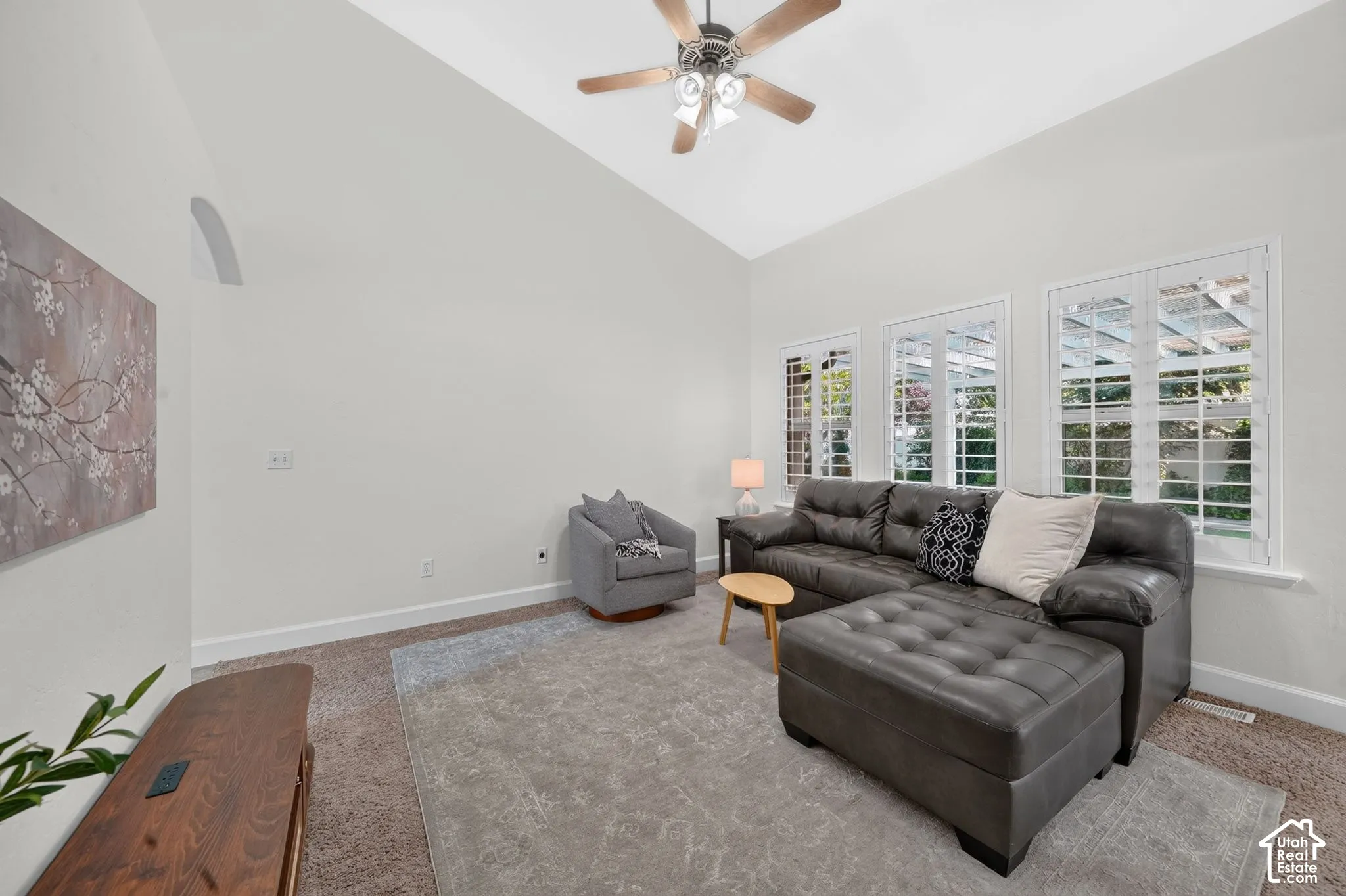 Vaulted ceiling, ceiling fan, multiple windows with plantation shutters, and light-toned walls