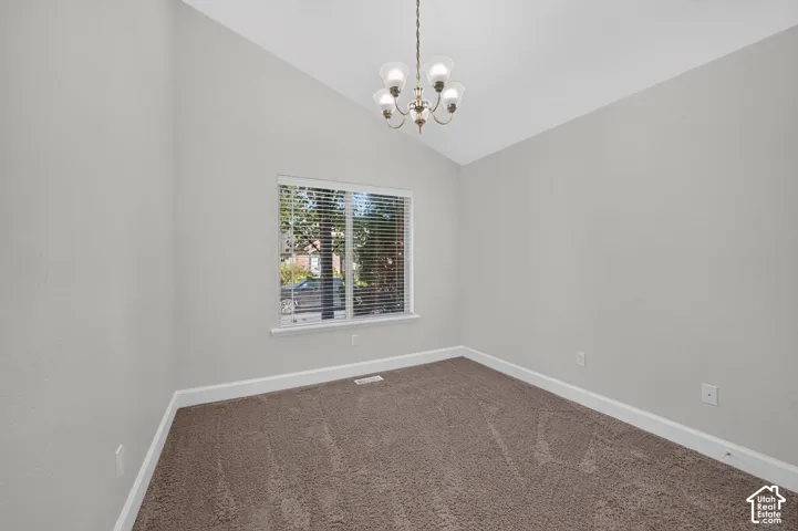 Vaulted ceiling, neutral wall paint, bronze chandelier, window with blinds, and carpeting