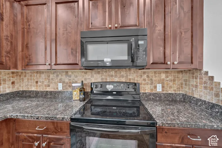 Dark wood-finish cabinetry, black over-the-range microwave, tile backsplash, and dark speckled countertops