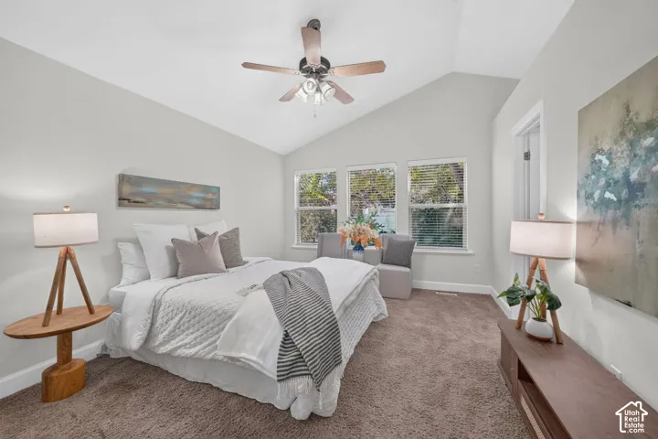 Vaulted ceiling with a ceiling fan, multiple windows, wall-to-wall carpeting, and white trim molding