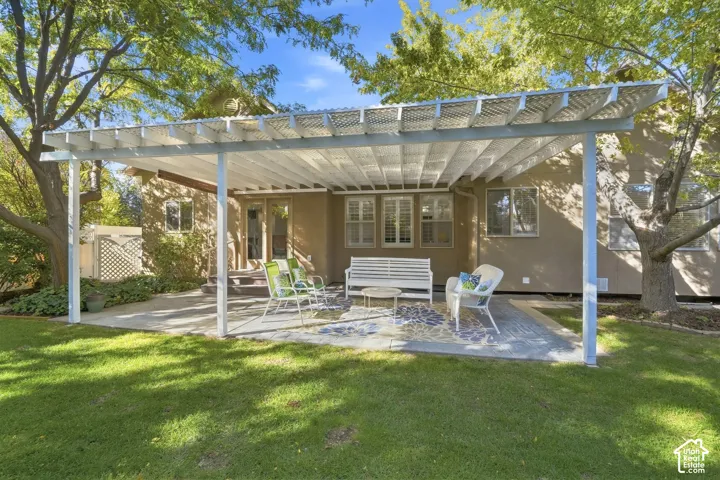 Expansive patio featuring a white pergola structure, concrete paving, and a manicured lawn
